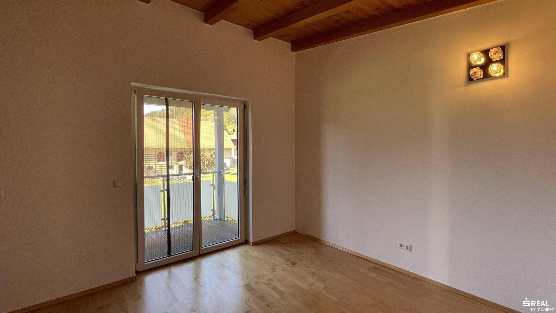Schlafzimmer mit Holzboden, Holzbalkendecke und direktem Zugang zum Balkon.