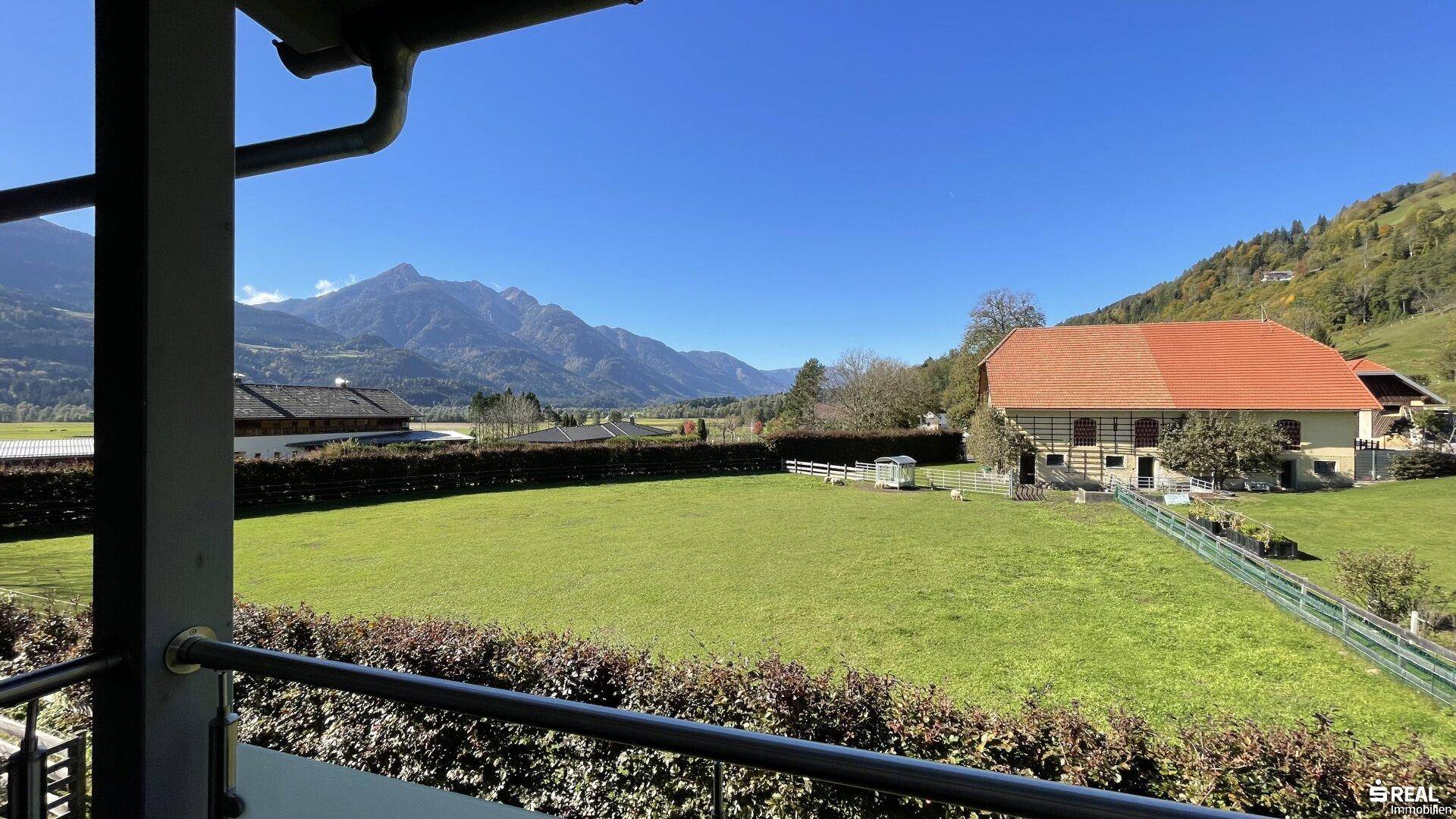 Weitläufiger Blick vom Balkon auf grüne Wiesen und die umliegende Berglandschaft.