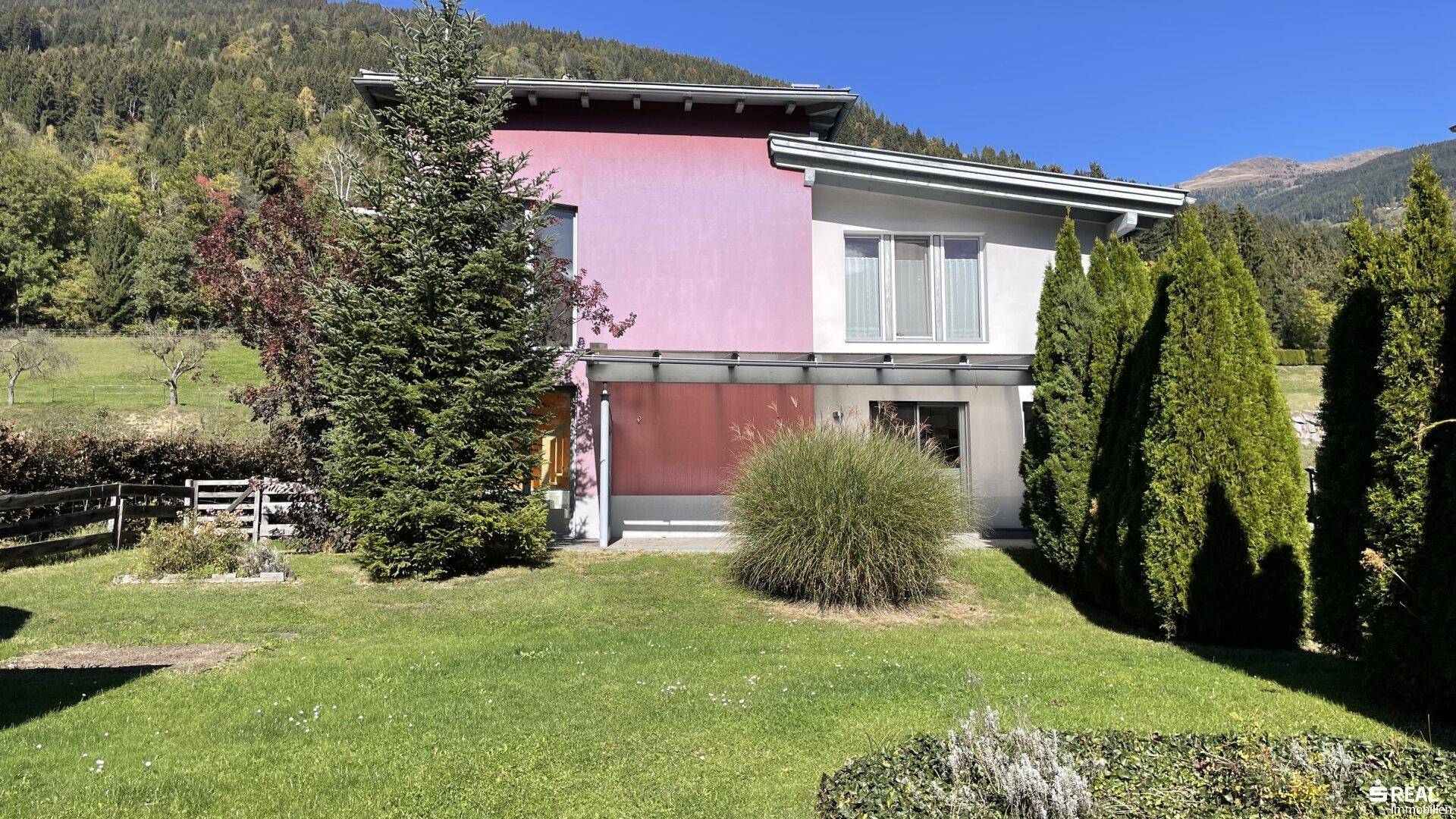 Modernes Einfamilienhaus mit farbiger Fassade, Garten und Bergblick.