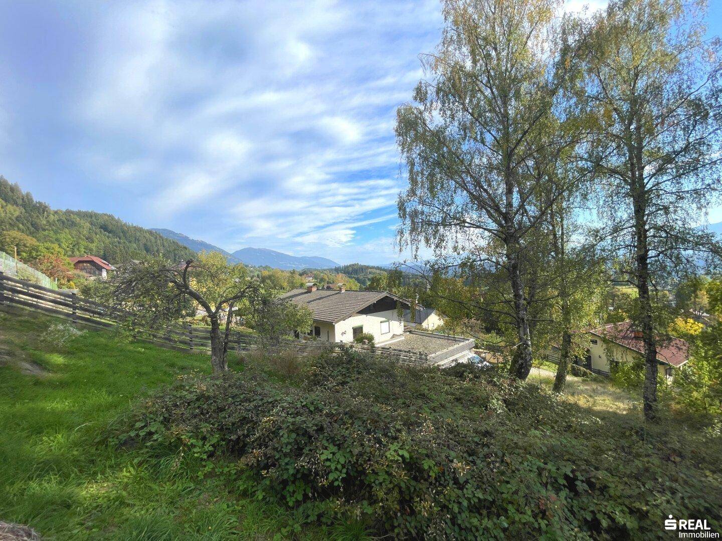 Haus umgeben von üppiger Vegetation und Bäumen, mit Bergpanorama in der Ferne.