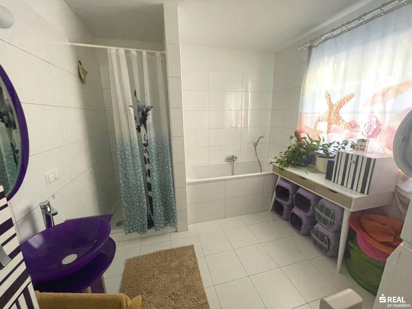 Helles Badezimmer mit Badewanne, Dusche, modernem lila Waschbecken und einem Fenster für Tageslicht.