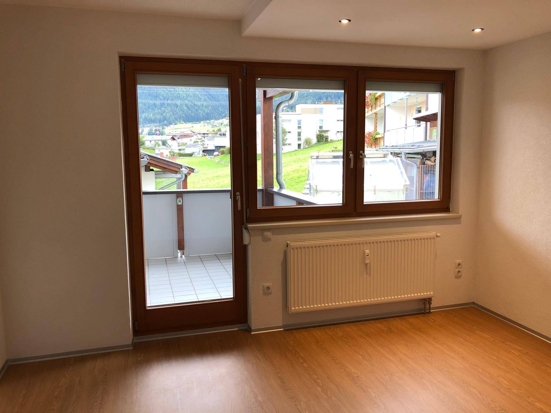 Geräumiges Zimmer mit Holzboden, großem Fenster und Balkonzugang mit Blick ins Grüne.