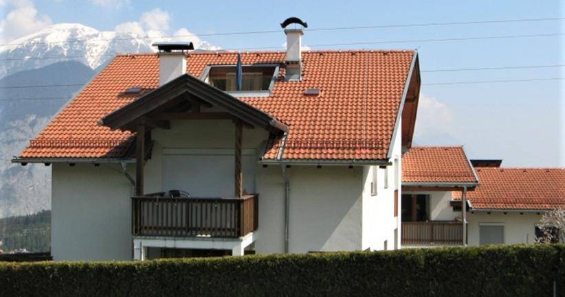 Traditionelles Haus mit rotem Ziegeldach, Balkon und beeindruckendem Bergblick im Hintergrund.