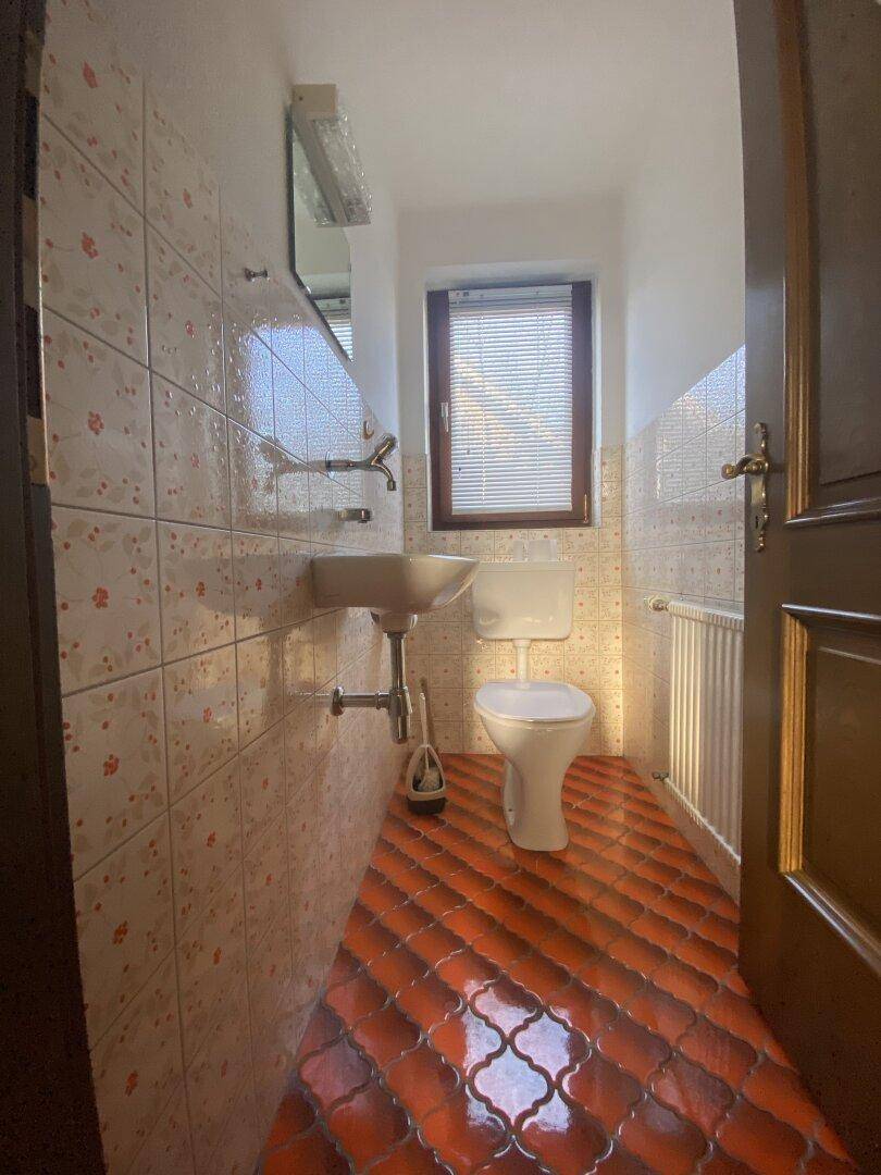 Kleines Gäste-WC mit Fenster, gefliestem Boden und Wänden in warmen Farbtönen.