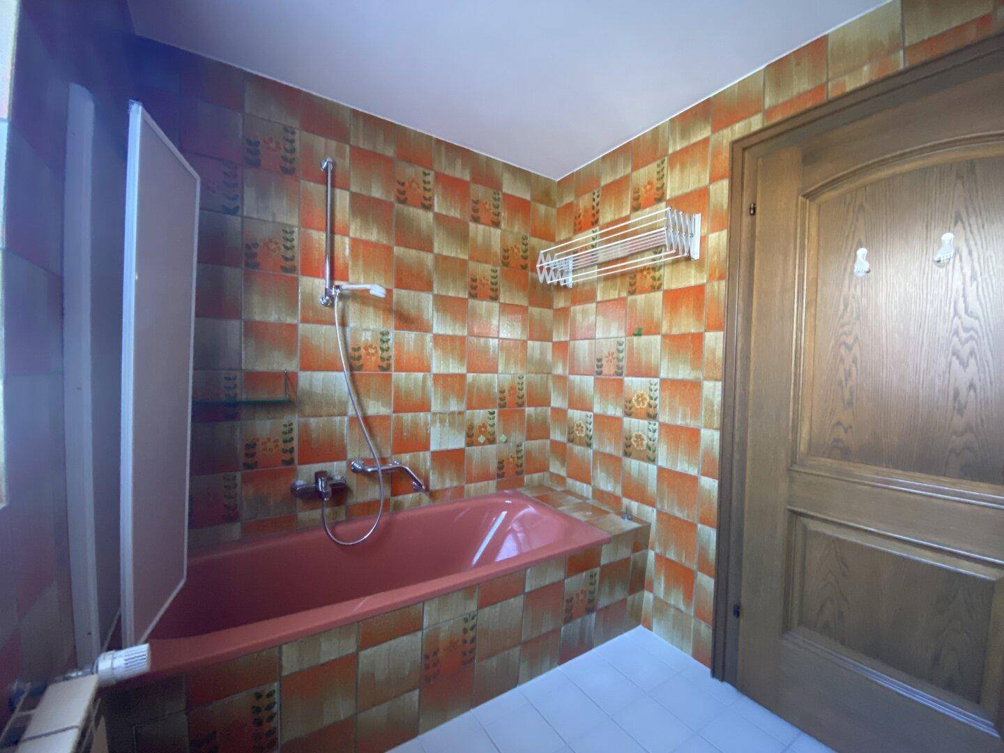 Badezimmer mit Badewanne und Duschvorrichtung, umgeben von gemusterten Wandfliesen.