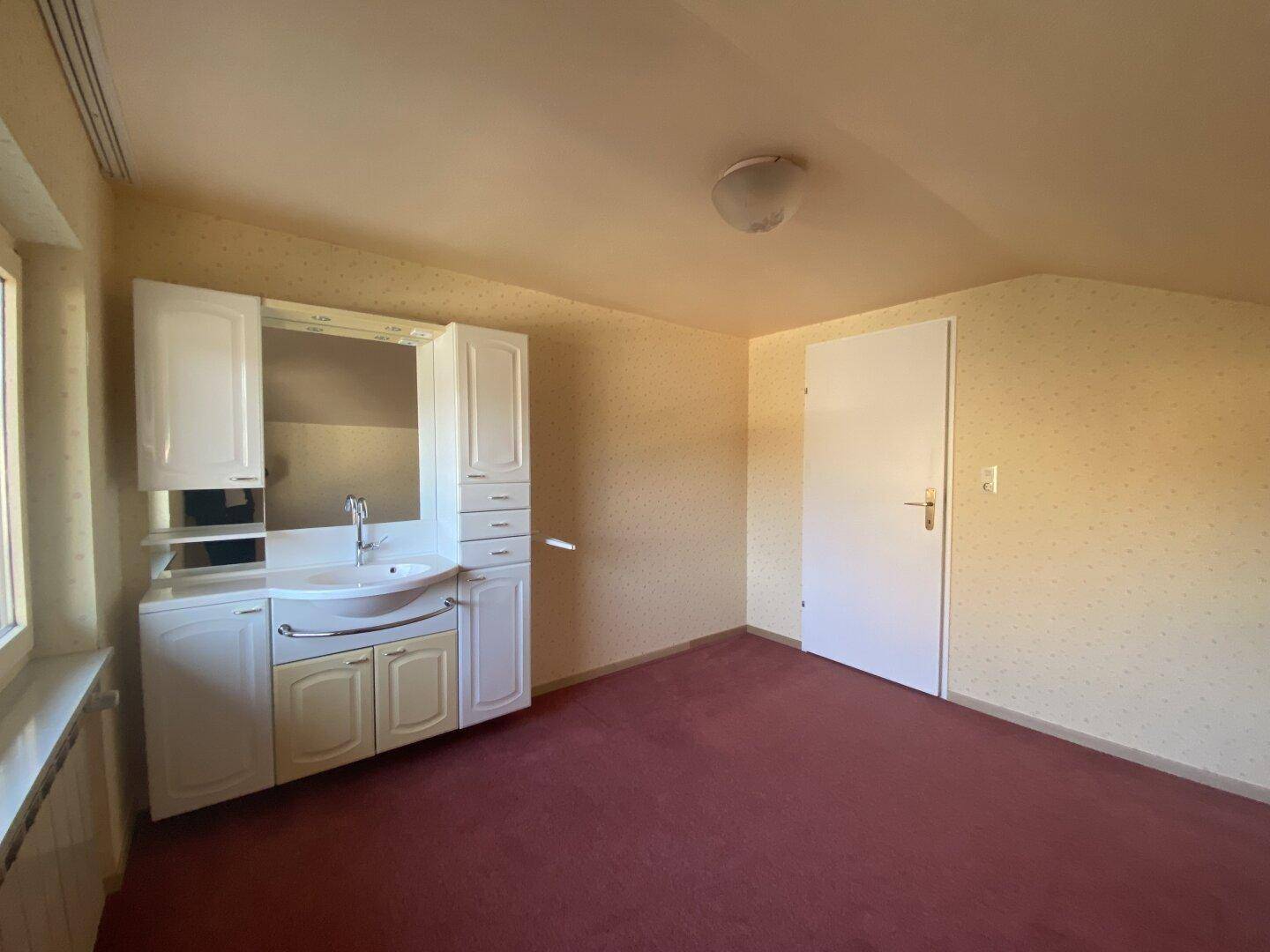 Dachzimmer mit Teppichboden, Fenster und einem Waschtisch mit Spiegelschrank.