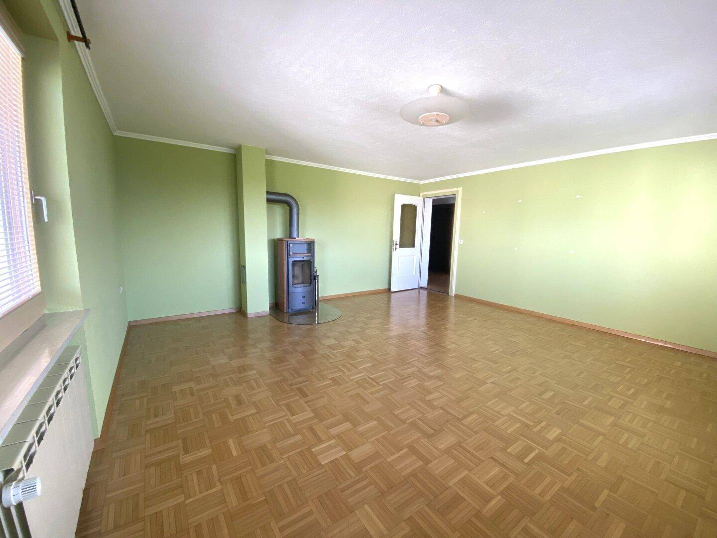 Gemütliches Wohnzimmer mit Parkettboden, grün gestrichenen Wänden und einem Kaminofen.