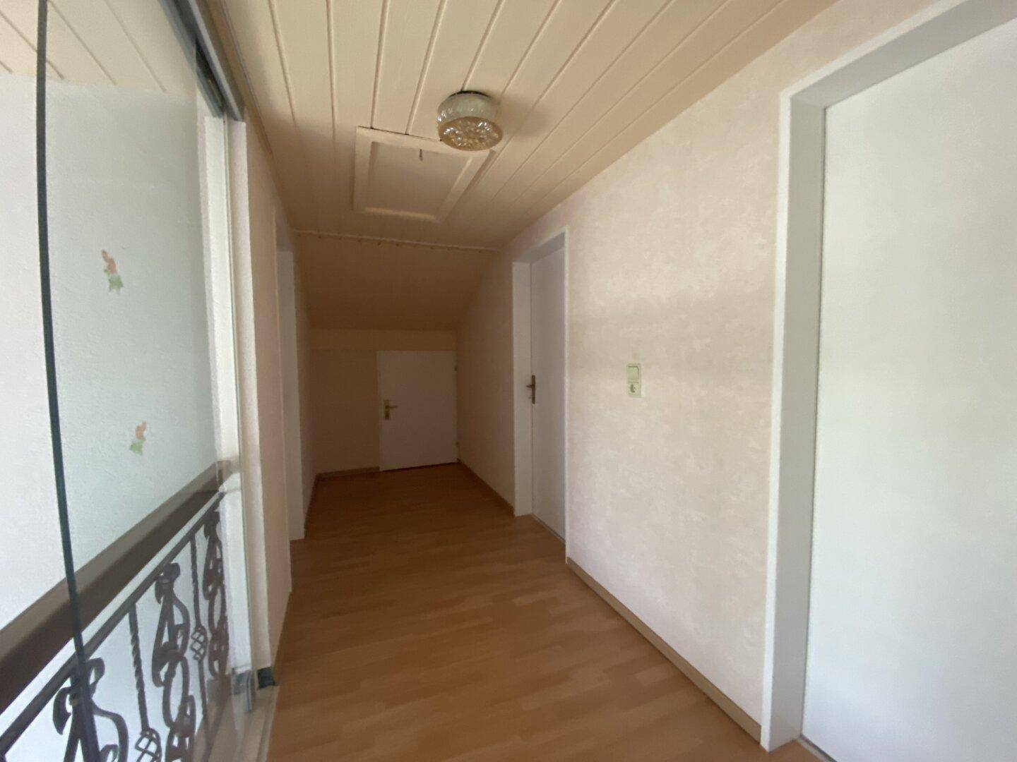 Dachgeschossflur mit Holzdeckenverkleidung und schrägen Wänden, der zu weiteren Räumen führt.