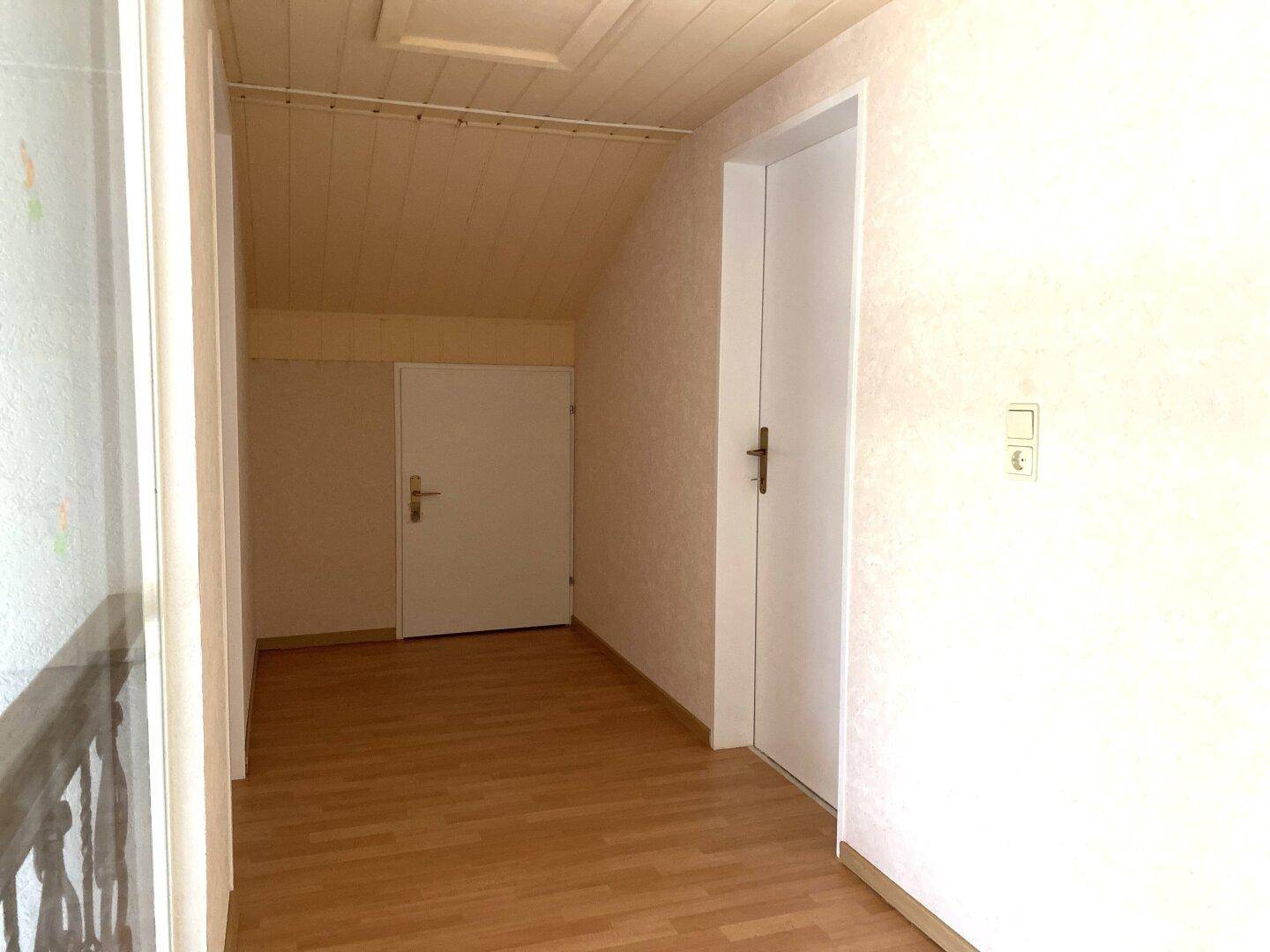 Dachgeschossflur mit schrägen Wänden und Holzboden, der den Zugang zu den Zimmern ermöglicht.