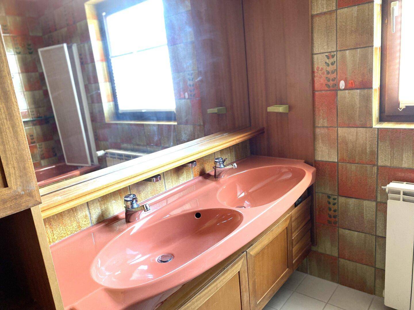 Badezimmer mit Doppelwaschbecken in Pastellrosa und gefliesten Wänden im 80er-Jahre-Stil.