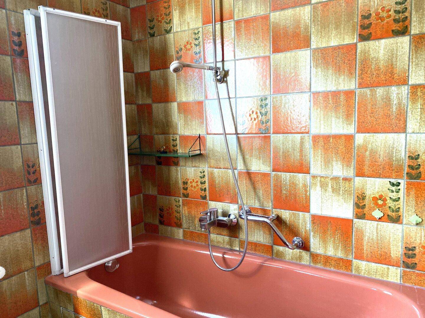 Badezimmer mit Badewanne in Pastellrosa und farbenfrohen Fliesen im Retro-Design.