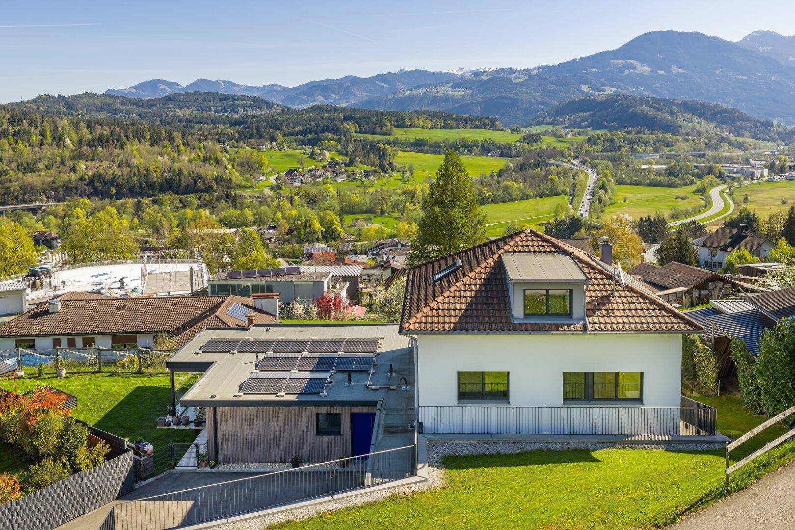 Modernes Haus mit Photovoltaikanlage auf dem Dach und weitem Bergblick in sonniger Lage.