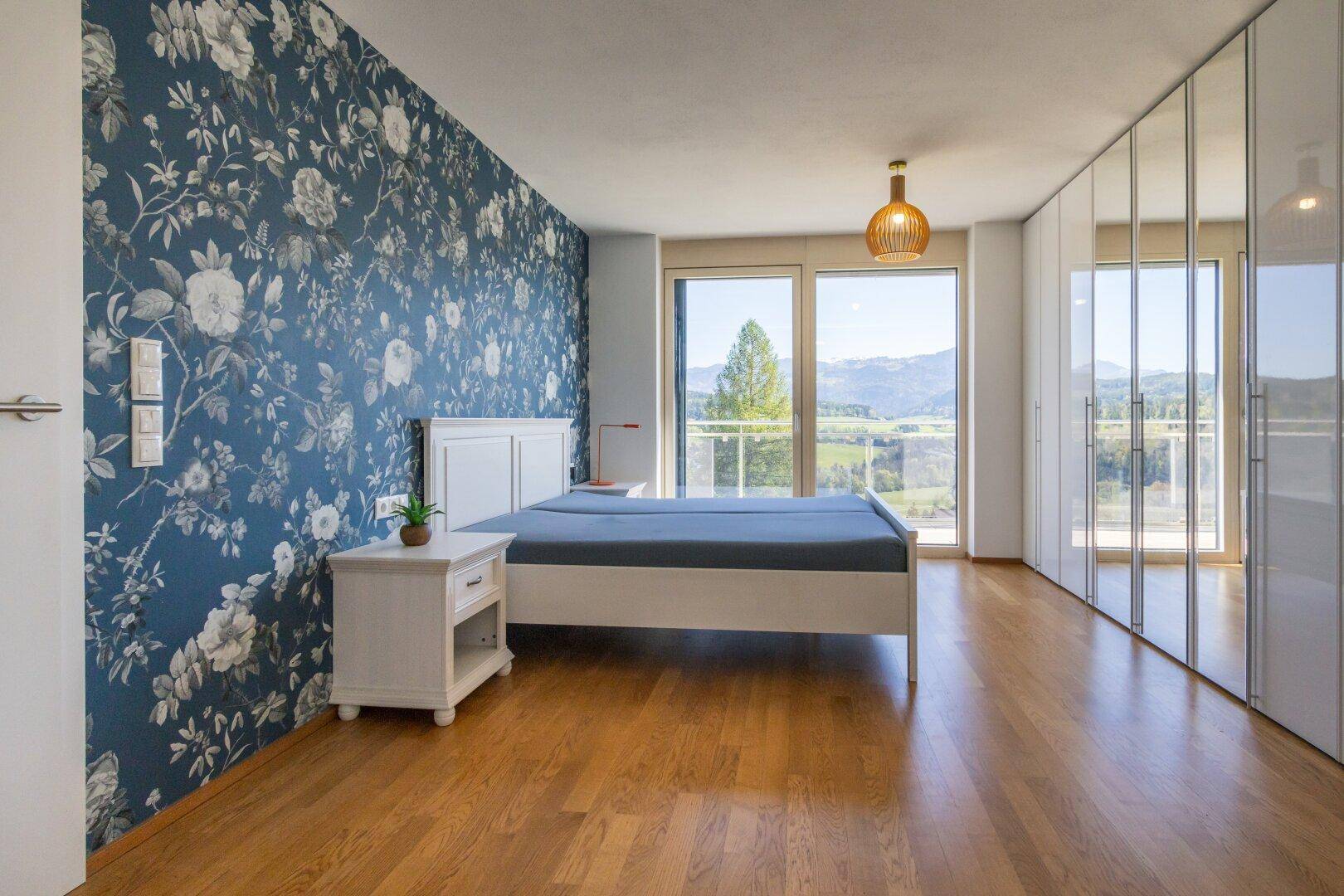 Geräumiges Schlafzimmer mit floraler Tapete, Spiegelschränken und Balkonzugang mit Bergblick.