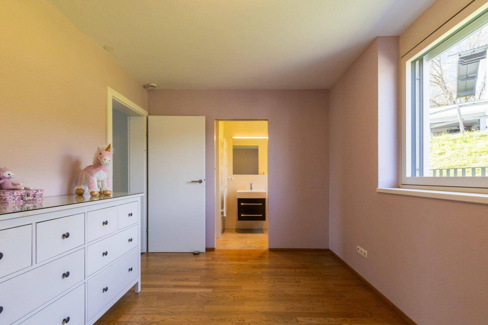 Kinderzimmer mit rosa Wänden, Holzboden und weißer Kommode in freundlicher Atmosphäre.