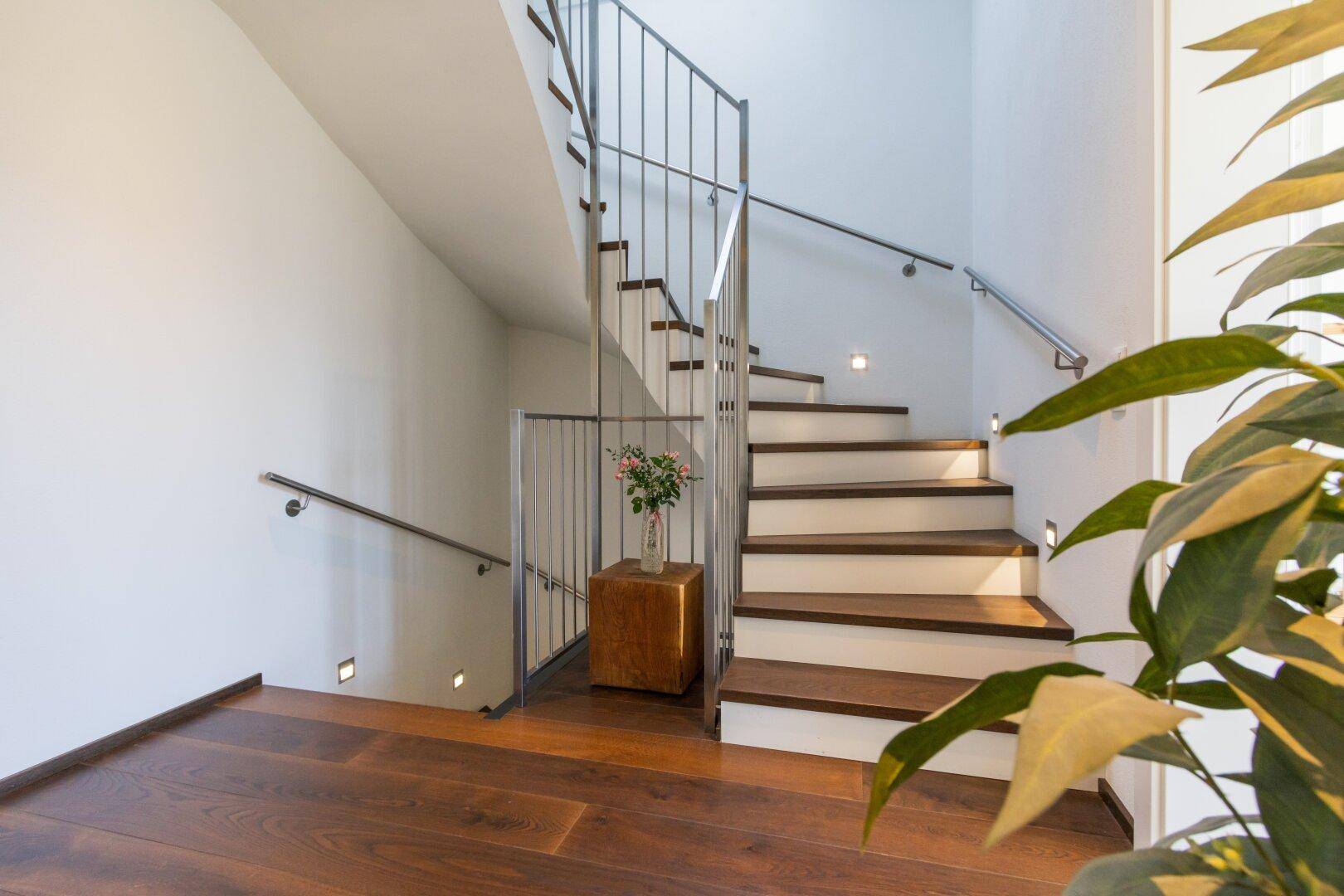 Elegante Holztreppe mit Edelstahlgeländer und indirekter Beleuchtung im Flur.