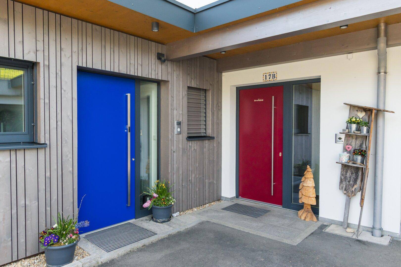 Zwei moderne Eingangstüren in leuchtendem Blau und Rot mit Holzverkleidung.