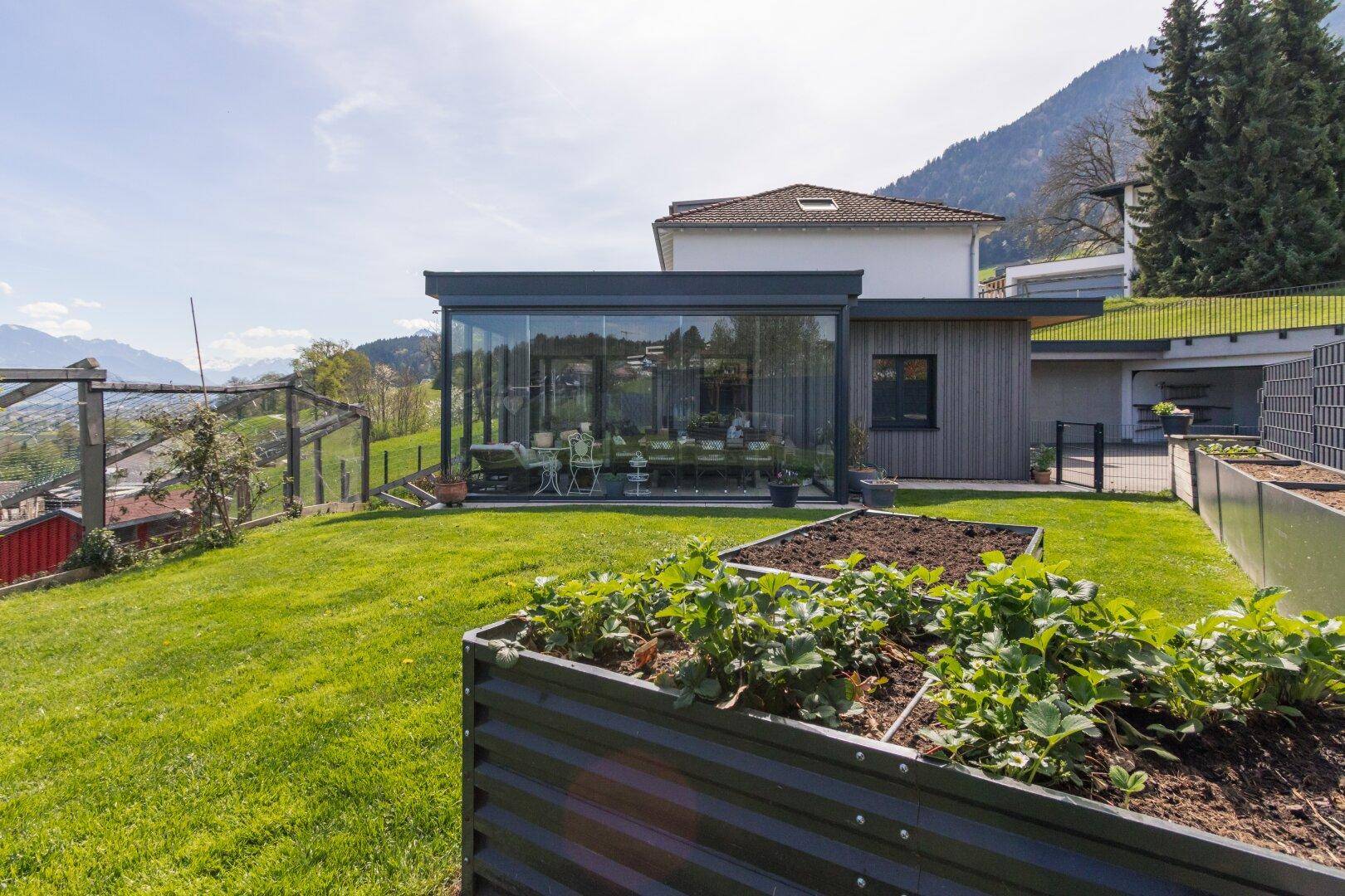 Gepflegter Garten mit Rasenfläche, Hochbeeten und Blick auf die umliegende Berglandschaft.