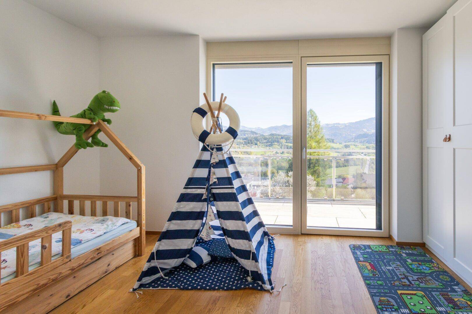 Helles Kinderzimmer mit Holzbett, Spielzelt und großen Fenstern mit Aussicht.