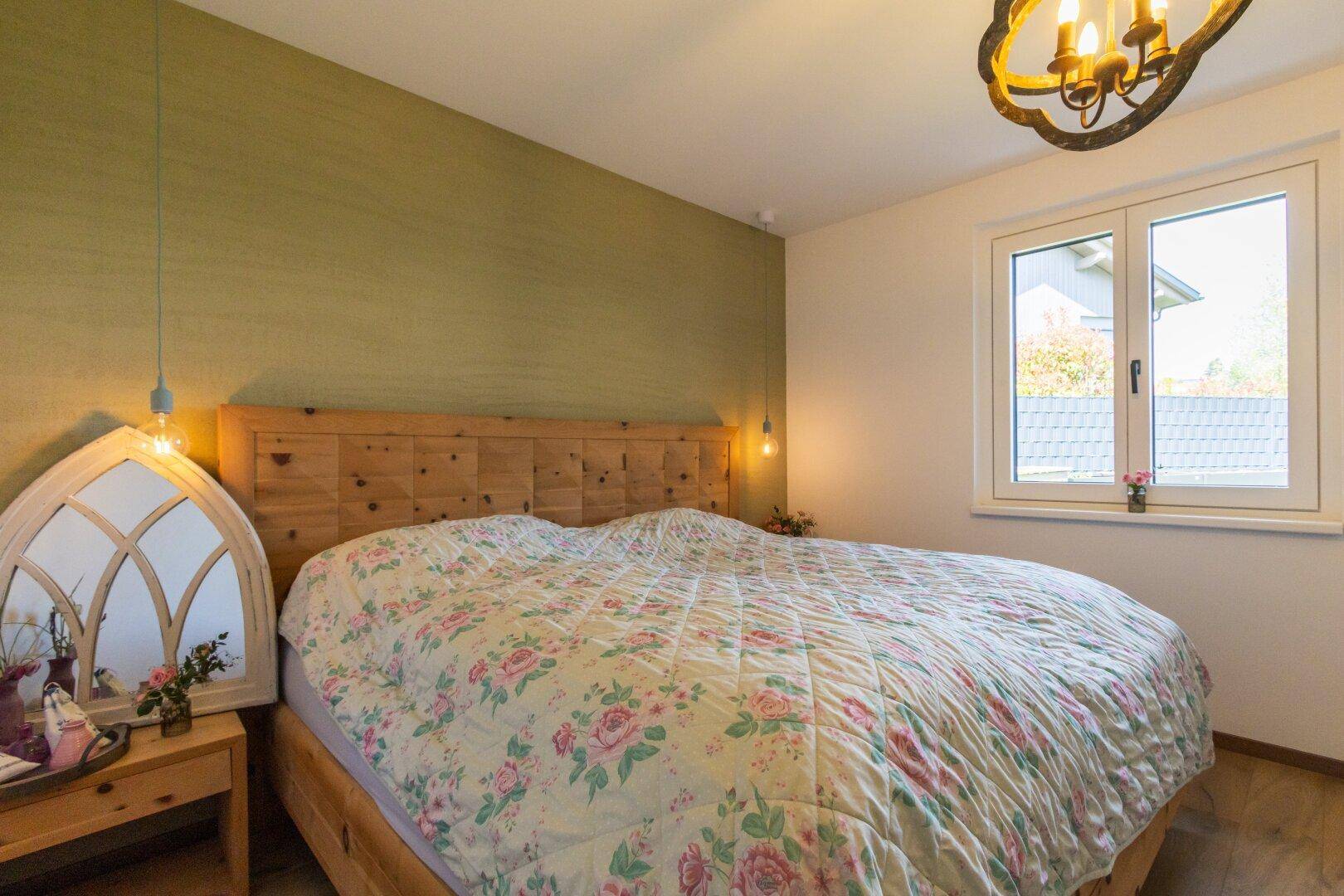 Gemütliches Schlafzimmer mit Holzbett, grüner Akzentwand und Fenster.