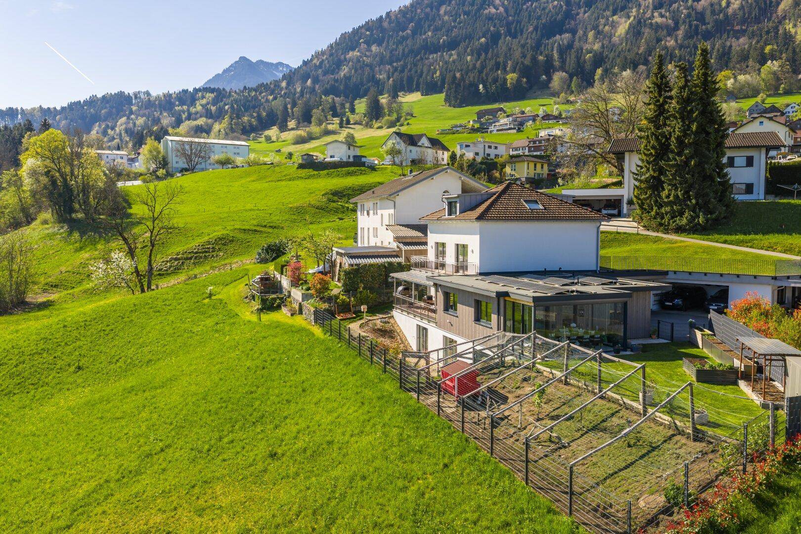 Weitläufige Luftaufnahme des Anwesens in grüner Hügellandschaft mit Bergblick.