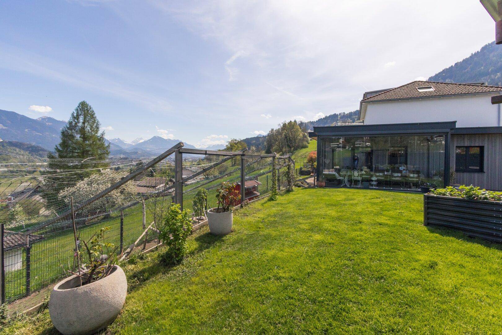 Garten mit Wintergarten und weitem Blick auf die umliegende Berglandschaft.