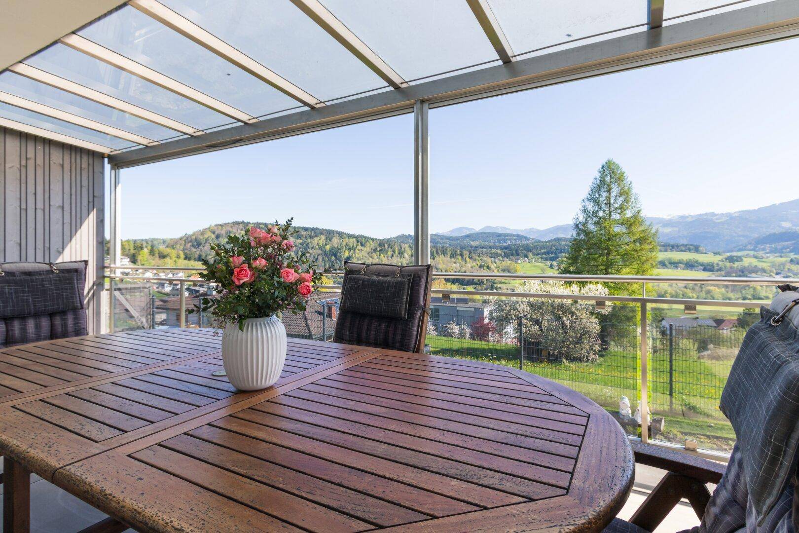 Überdachte Terrasse mit Holztisch, Sitzgelegenheiten und weitem Blick auf die grüne Landschaft.