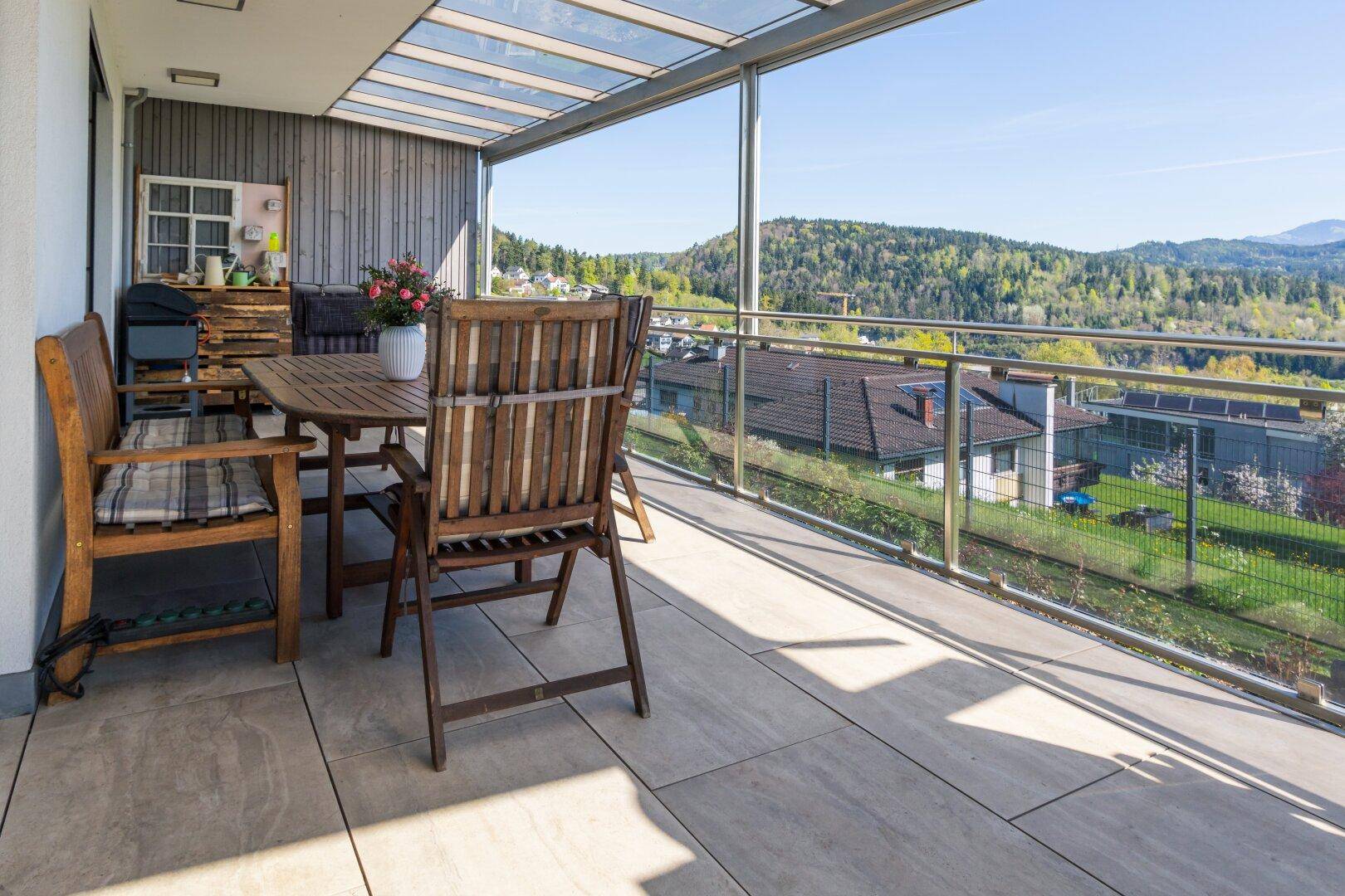 Helle Terrasse mit Holztisch, Stühlen und weitem Blick über die hügelige Landschaft.