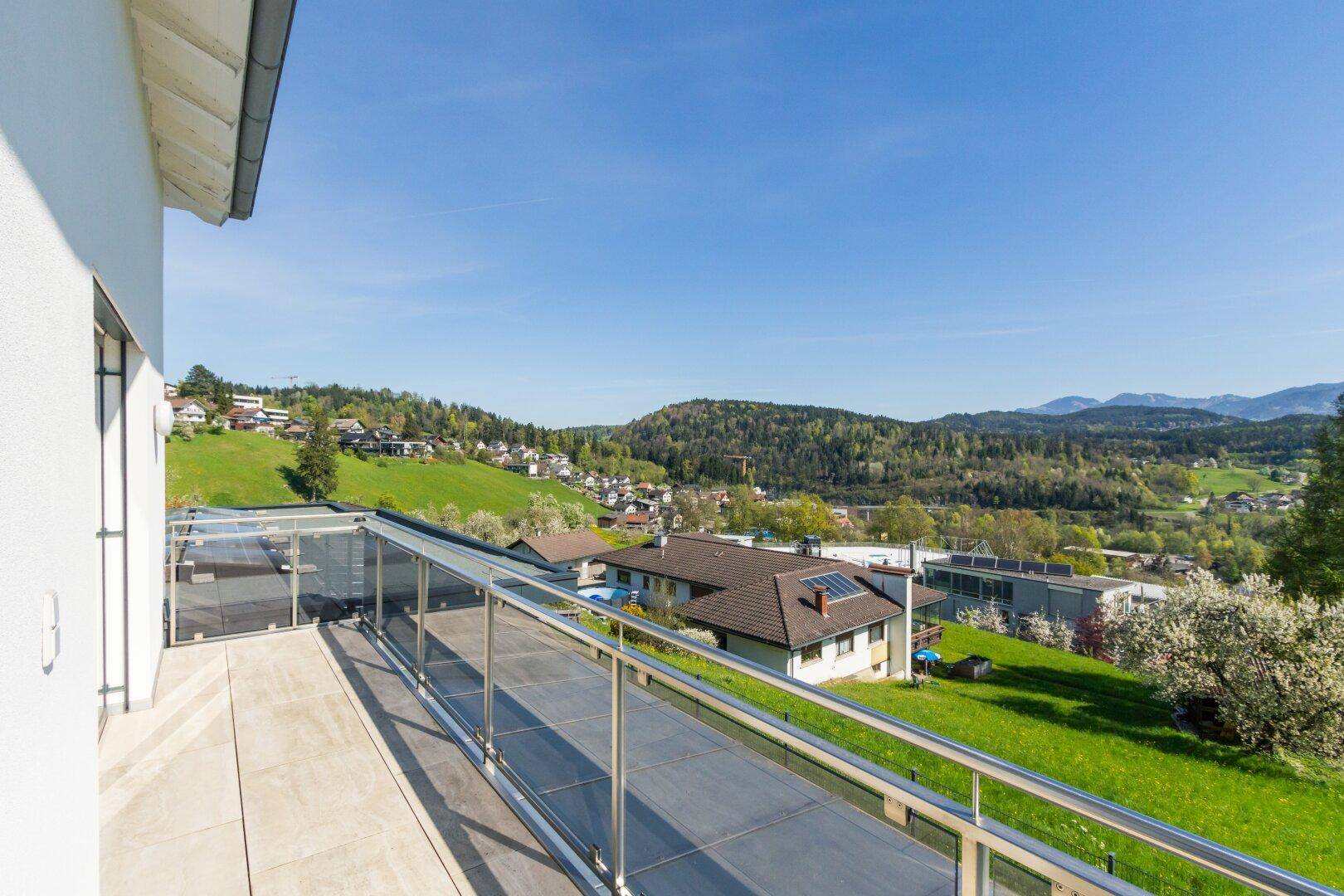 Geräumiger Balkon mit Glasgeländer und weitem Blick über die grüne Landschaft.