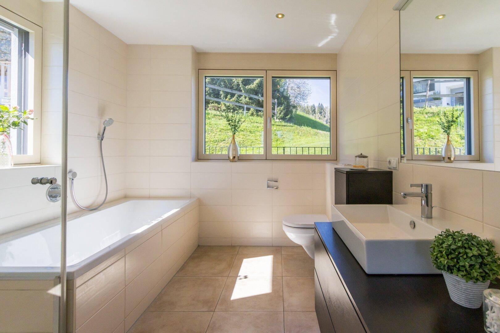 Modernes Badezimmer mit Badewanne, Waschbecken und Fenster mit Blick ins Grüne.