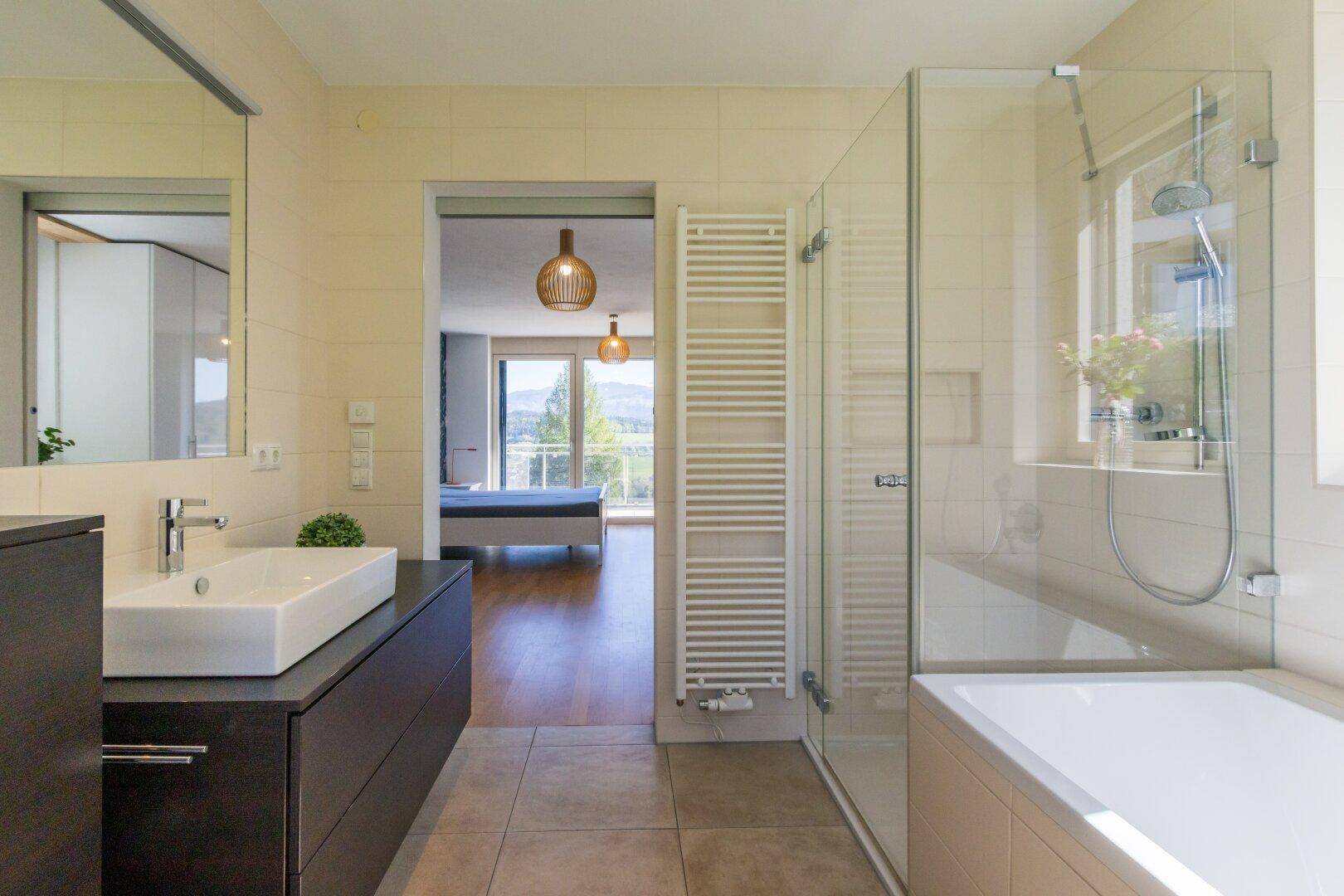 Helles Badezimmer mit Dusche, Waschbecken und Zugang zum angrenzenden Schlafzimmer.