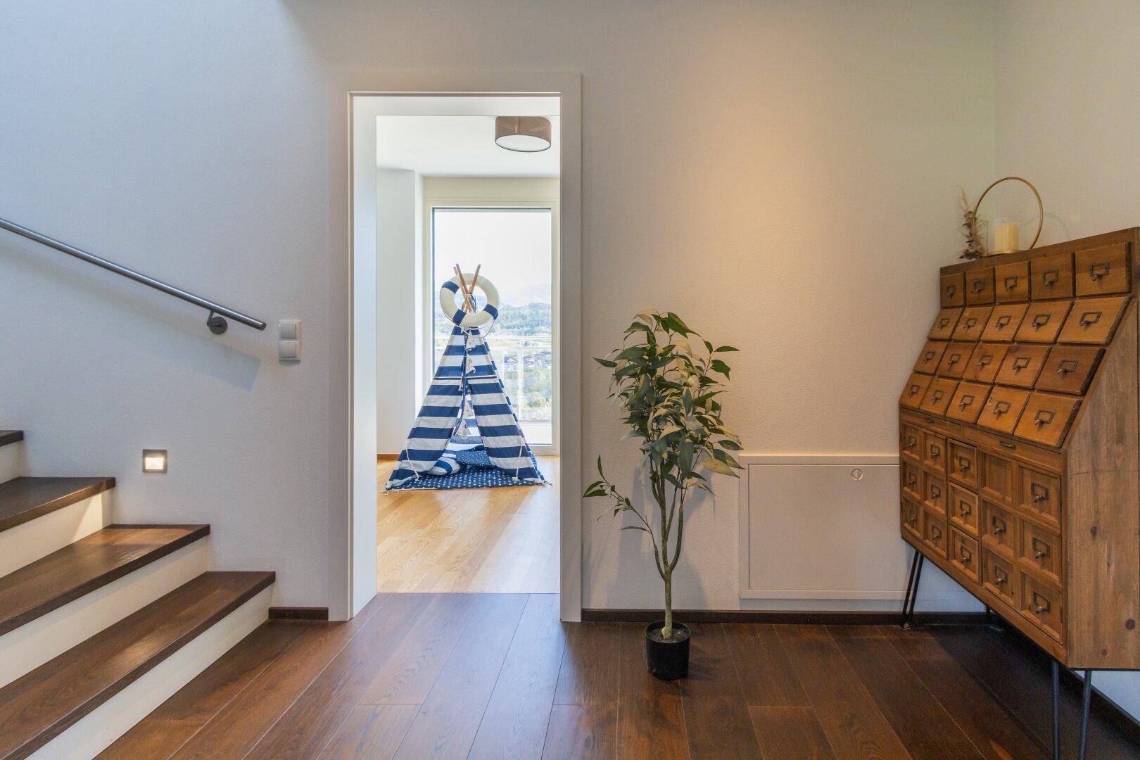 Heller Flur mit Holztreppe, modernem Geländer und Zugang zu einem weiteren Zimmer.