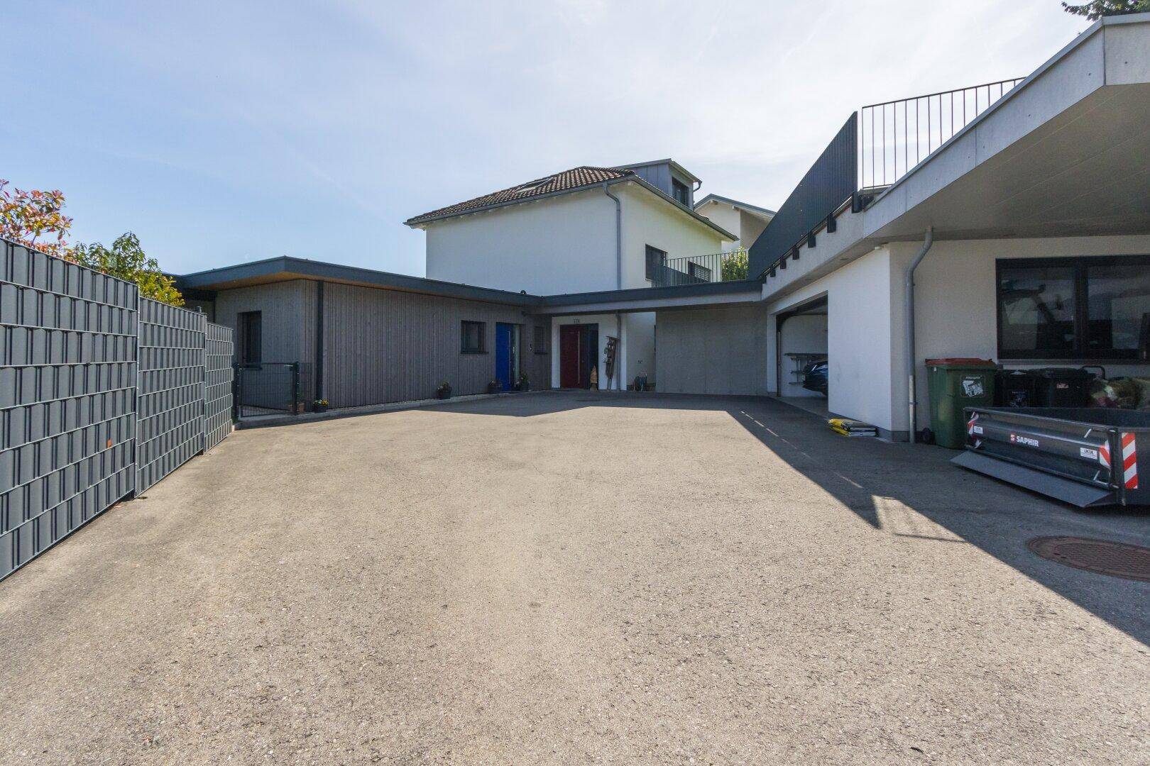 Großer gepflasterter Vorplatz mit Carport und Zufahrt zu den Gebäuden, umgeben von Natur.