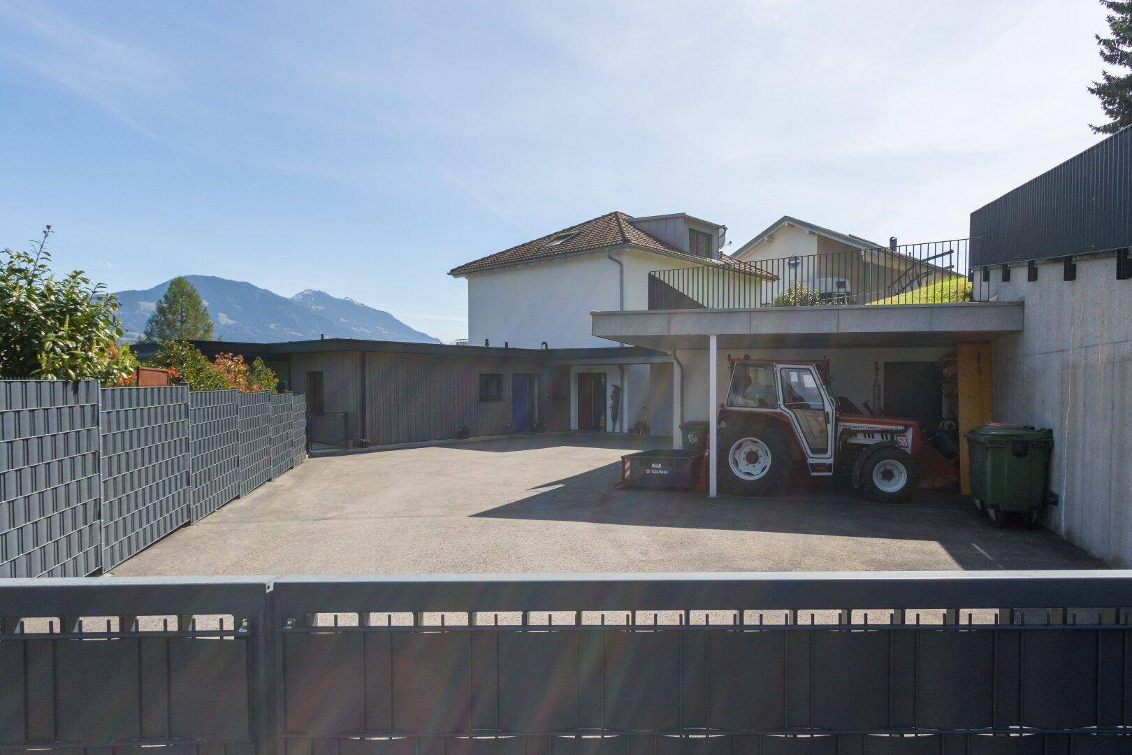Weitläufiger Außenbereich mit großem Hof, Carport und Blick auf die umliegende Berglandschaft.