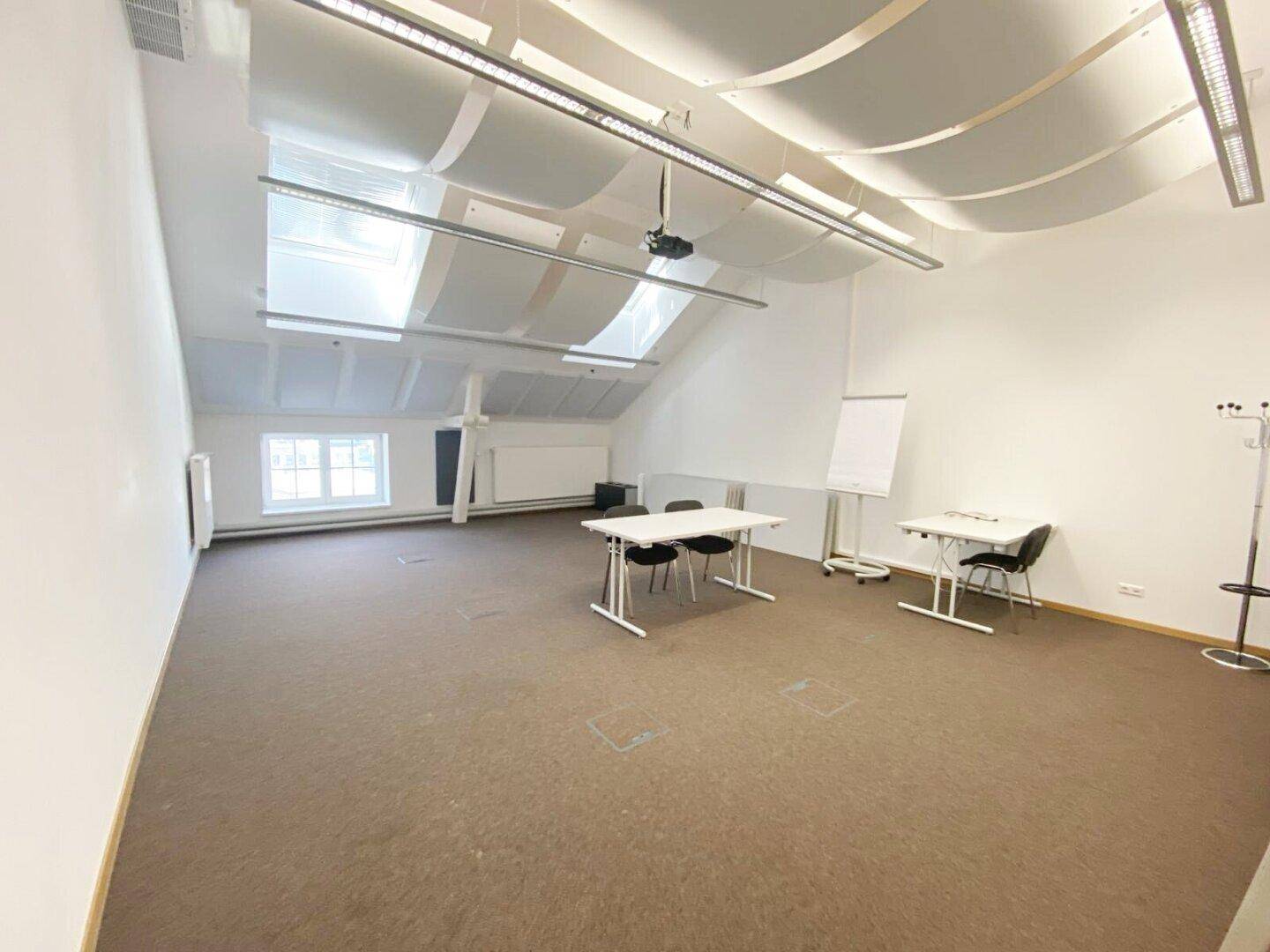 Großer Konferenzraum im Dachgeschoss mit Teppichboden, Dachfenstern und einem Projektor für Präsentationen.