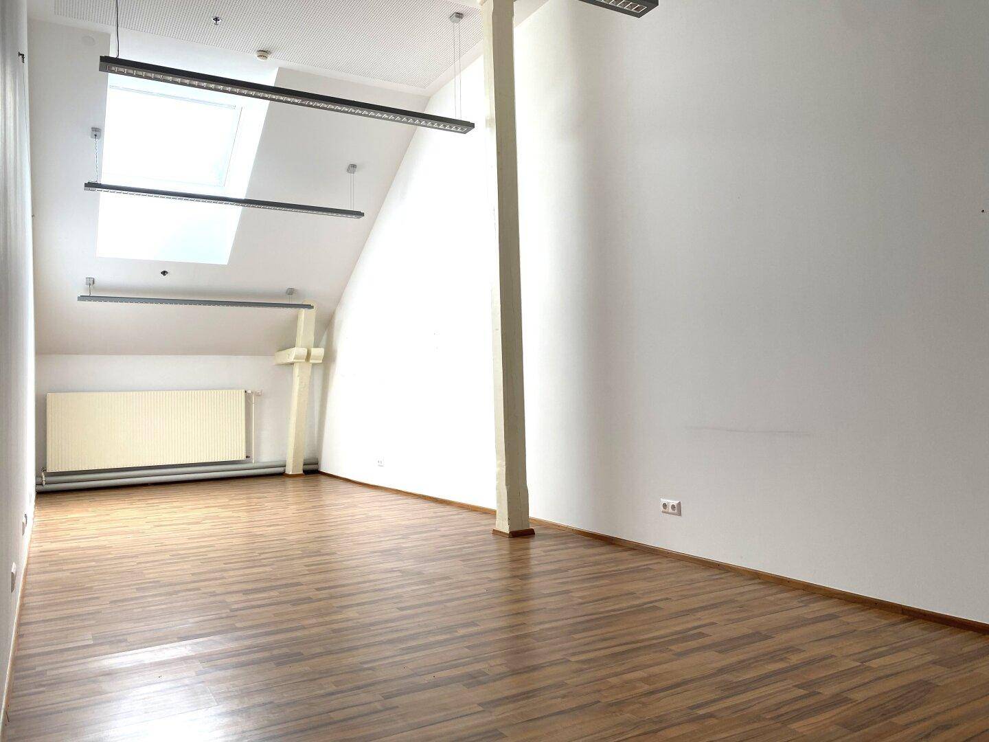 Heller Büroraum im Dachgeschoss mit Holzboden, Dachfenster und Heizkörper, ideal für ruhiges Arbeiten.