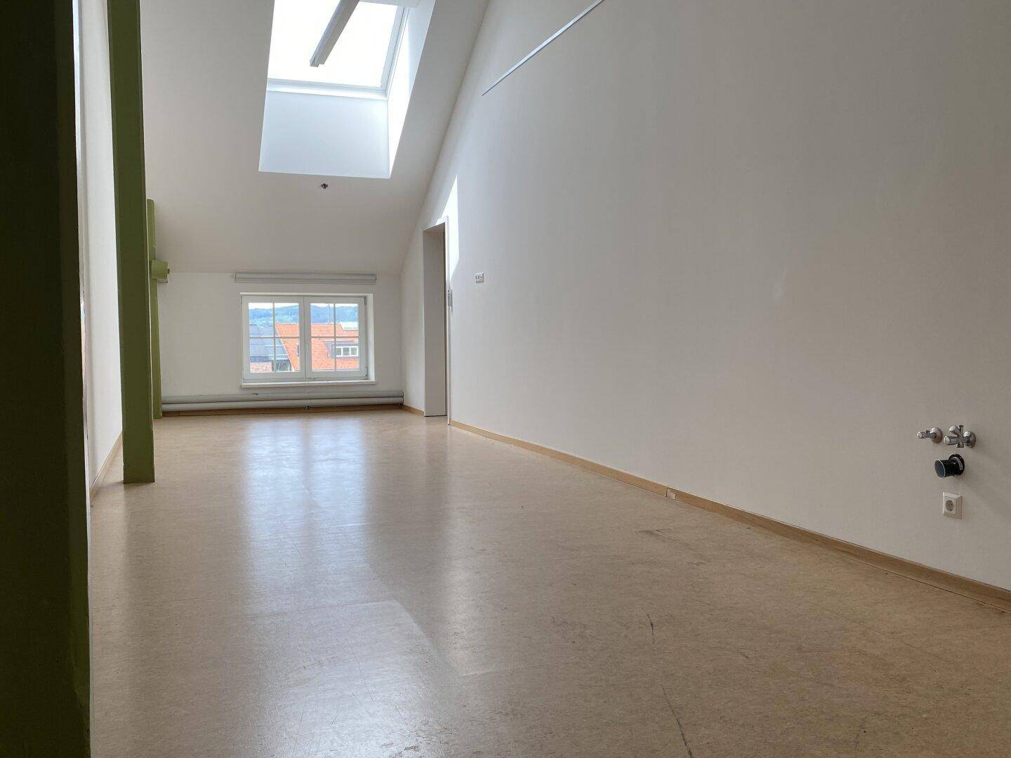 Geräumiger, leerer Raum mit Linoleumboden und Fenster, das einen Blick auf die Umgebung bietet.