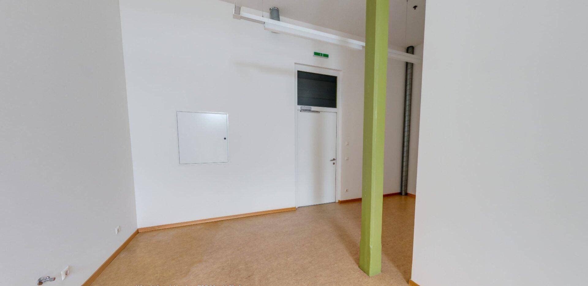 Heller, leerer Raum mit Linoleumboden und einem auffälligen grünen Pfeiler, bereit zur Nutzung.