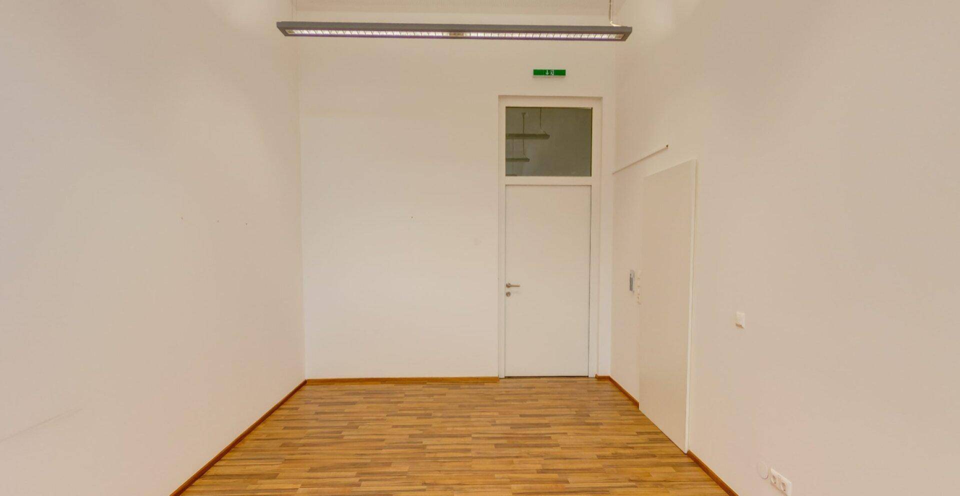 Heller, leerer Raum mit Holzboden und einer Tür, die zu einem weiteren Bereich führt, ideal für Büronutzung.