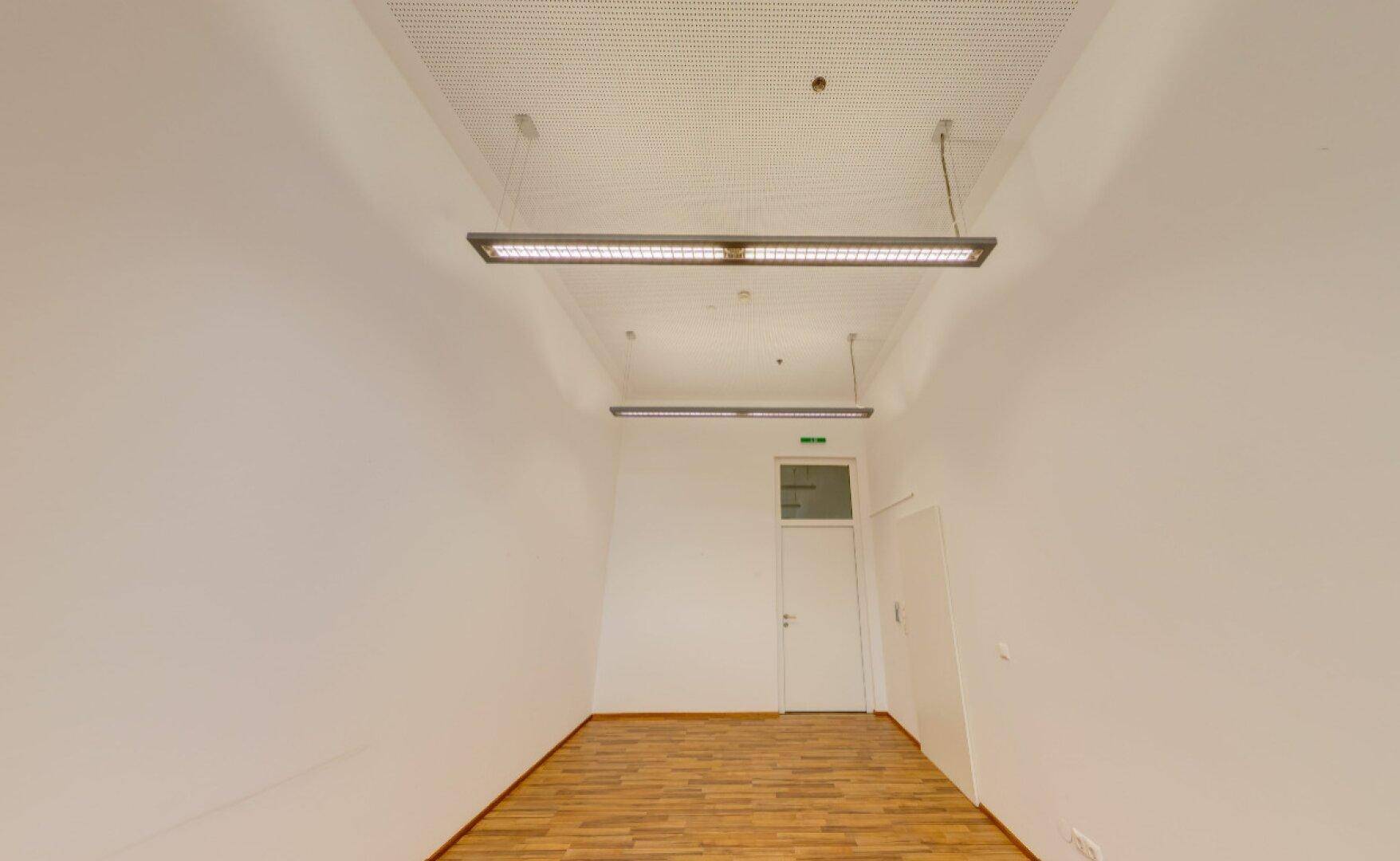 Leerer Büroraum mit Holzboden und modernen Deckenleuchten, ideal für flexible Arbeitsplatzgestaltung.