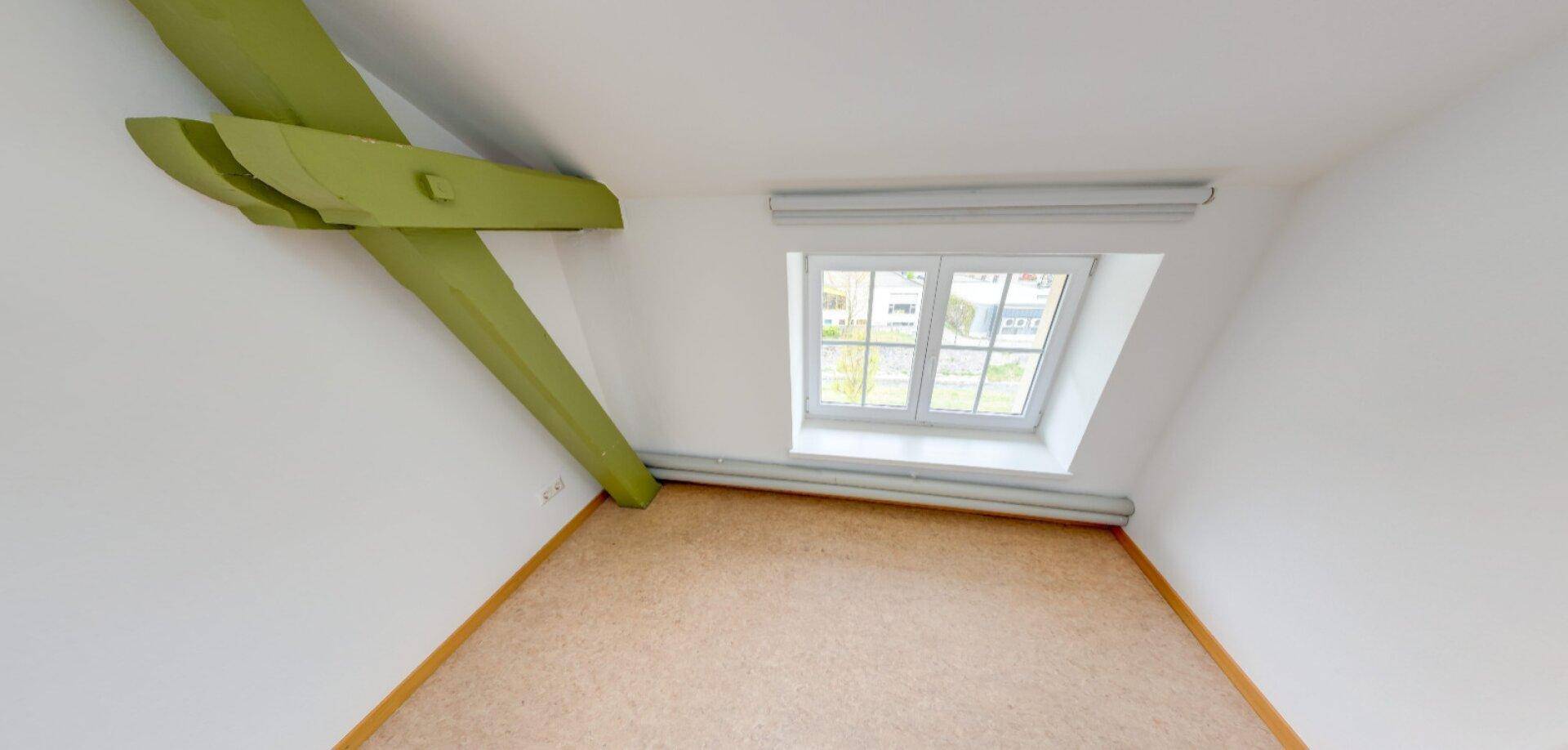 Kleiner Büroraum im Dachgeschoss mit Linoleumboden, Fenster und einem markanten grünen Holzbalken.