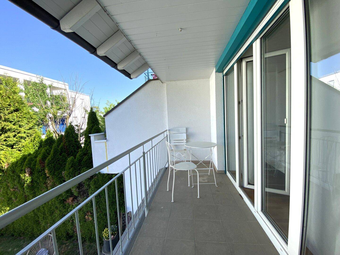 Sonniger Balkon mit Sitzgelegenheit und Blick ins Grüne.