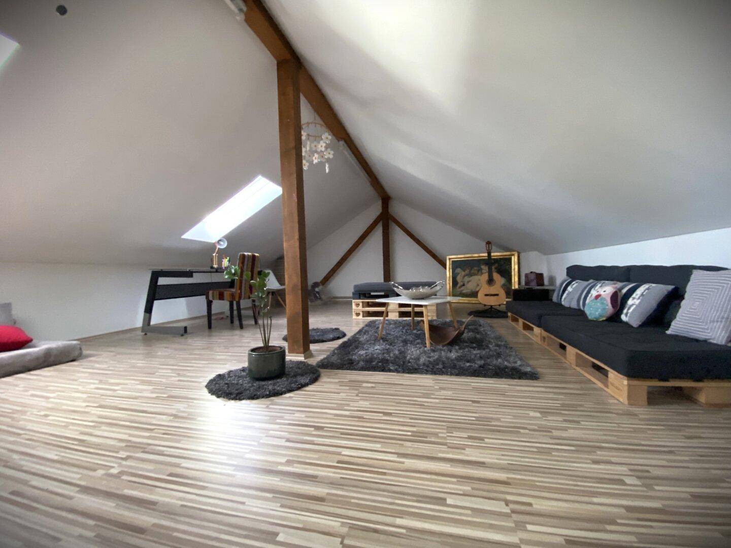 Geräumiger Dachboden als Wohnbereich mit Dachschrägen, Holzbalken und Laminatboden.