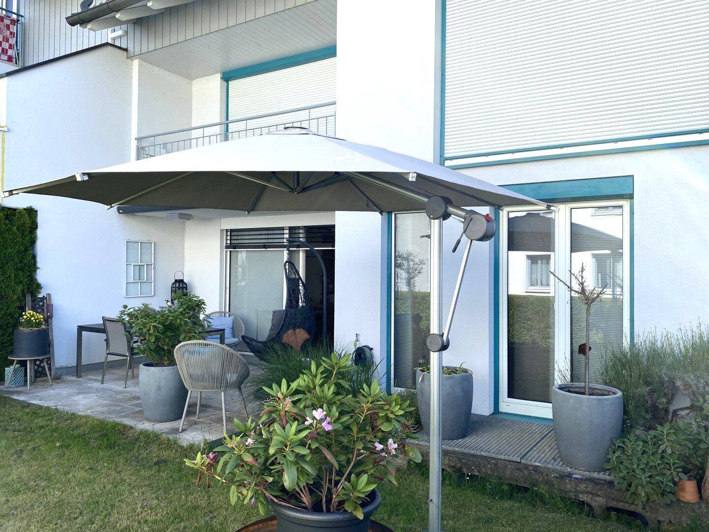 Möblierte Terrasse mit großem Sonnenschirm und Blick auf den grünen Gartenbereich des Hauses.