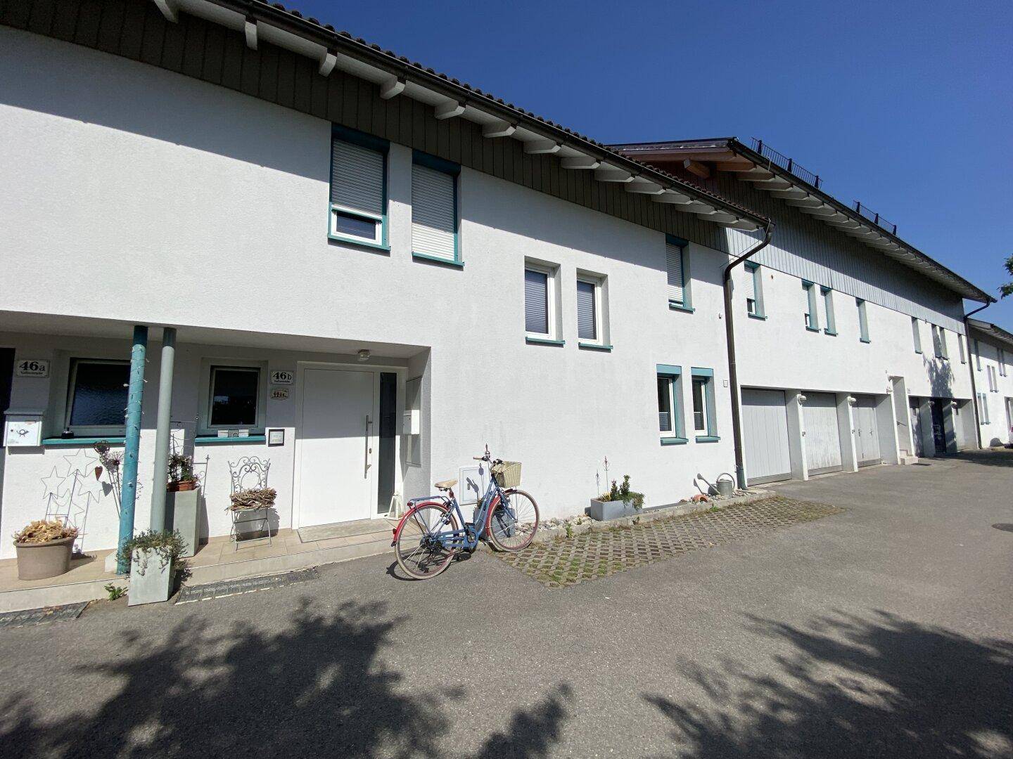 Reihenhausfassade mit weißen Wänden, blauen Akzenten und Garagenzugängen entlang der Straße.