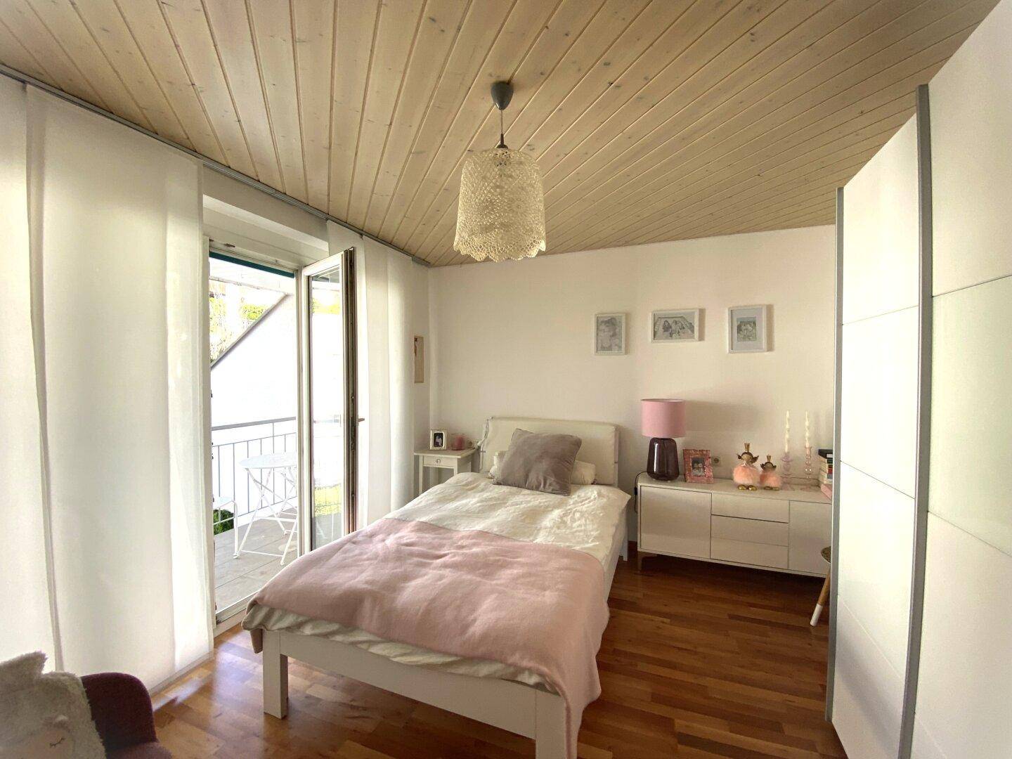 Helles Schlafzimmer mit Holzbalkendecke, Einzelbett und Balkonzugang.
