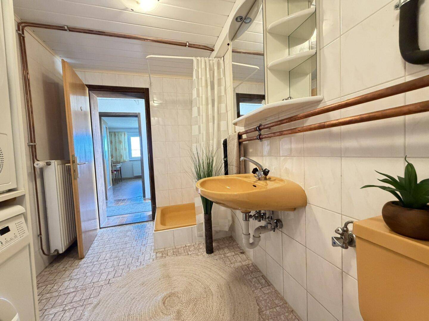 Badezimmer im 80er-Jahre-Stil mit gelbem Waschbecken, Dusche und Fliesenboden.