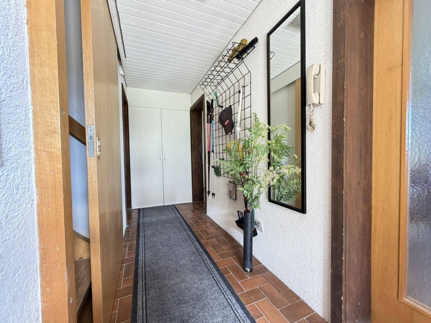 Heller Flur mit Terrakotta-Fliesenboden, Spiegel und Garderobe.