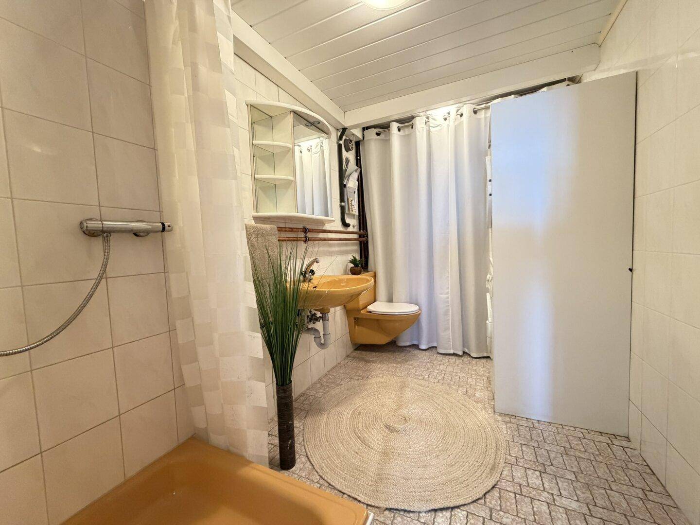 Funktionales Badezimmer mit Duschbereich, WC und runder Badematte.