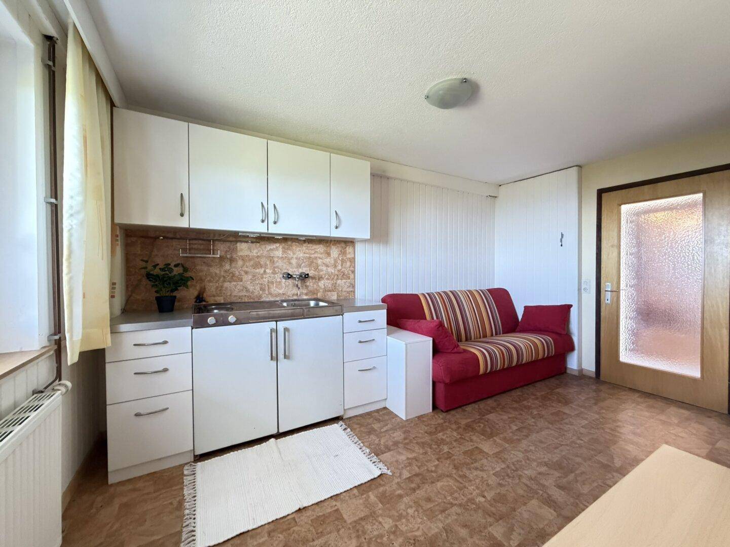 Kleiner Wohnbereich mit integrierter Küchenzeile und rotem Sofa, ideal für Singles.