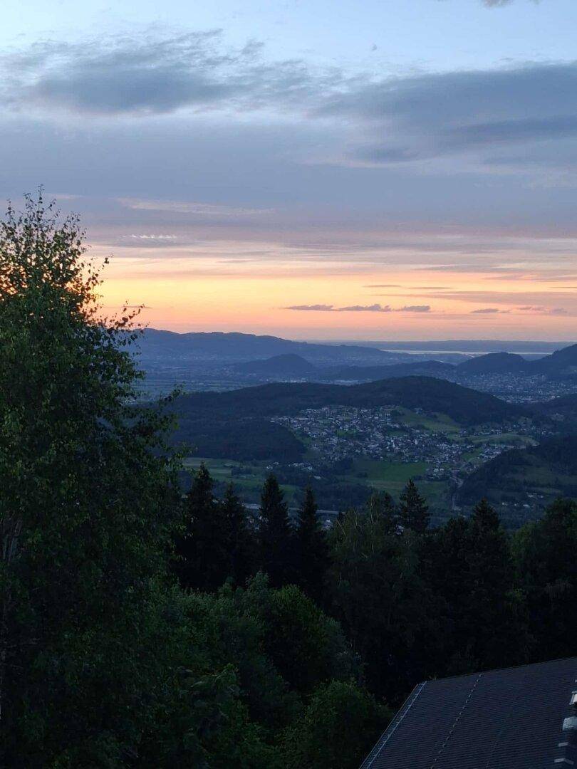 Malerischer Sonnenuntergang über einem Tal mit fernen Ortschaften und Bergen.